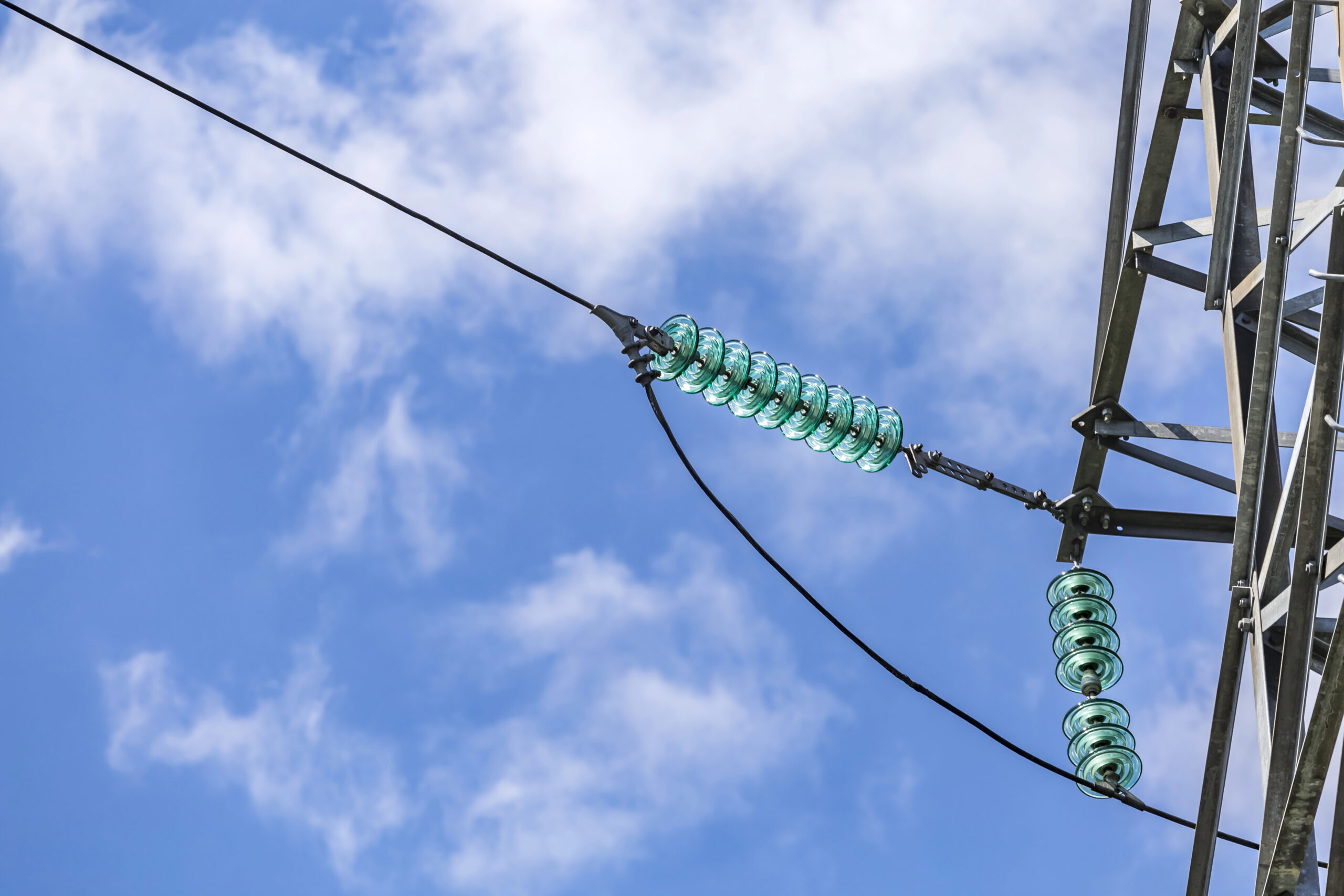 Close up of a transparent turquoise high voltage insulator or isolator in sunlight on electric tower on blue sky background